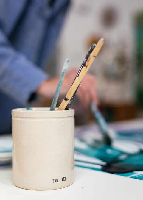 A collection of used paintbrushes in a ceramic jar