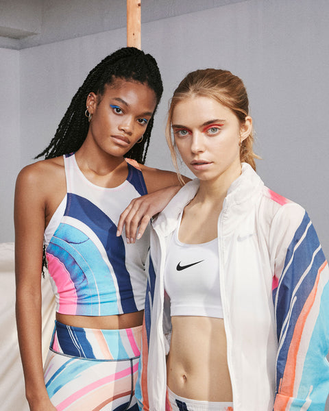 Two women wearing Nike athletic clothing with prints designed by Eva featuring arched stripes in blues and pinks on a white background