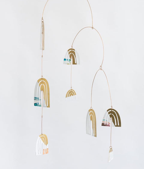 A delicate, hanging mobile with flat, arched objects with cut outs and abstract shapes printed on the surface