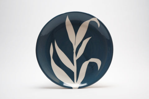 Navy blue ceramic plate with a cream silhouette of leaves as a focal design element