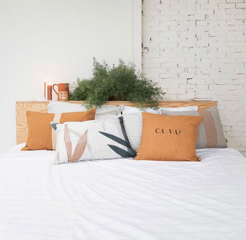 Bed styled with pillows including one designed by Eva with two silhouettes of leaves against a white background