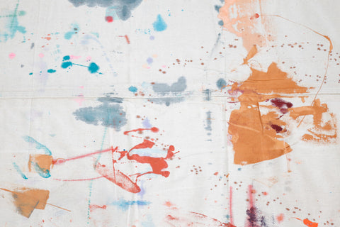 A piece of white dropcloth with splatters and dried puddles of a variety of paint colors